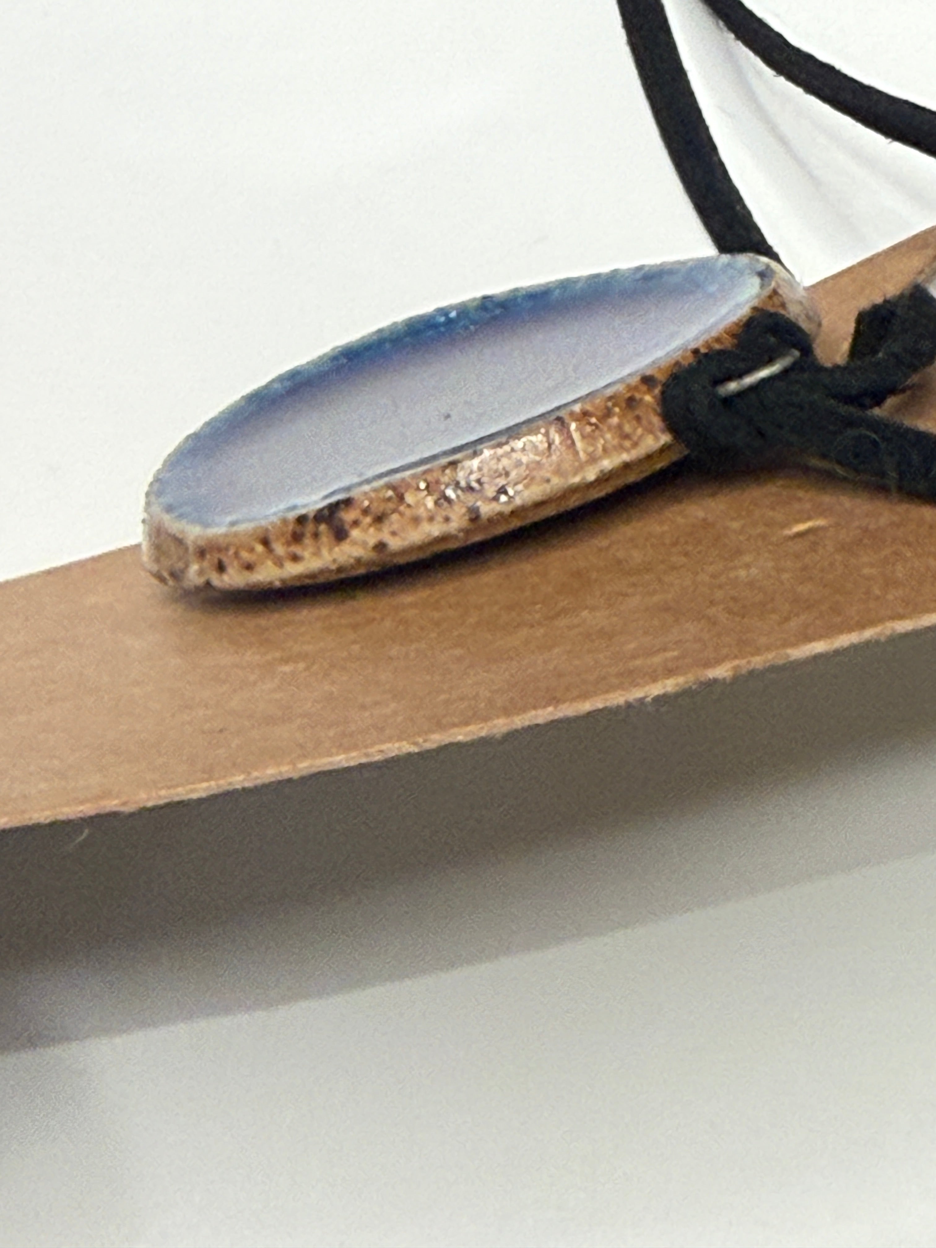 Close-up of a necklace with a blue pendant on a neutral background