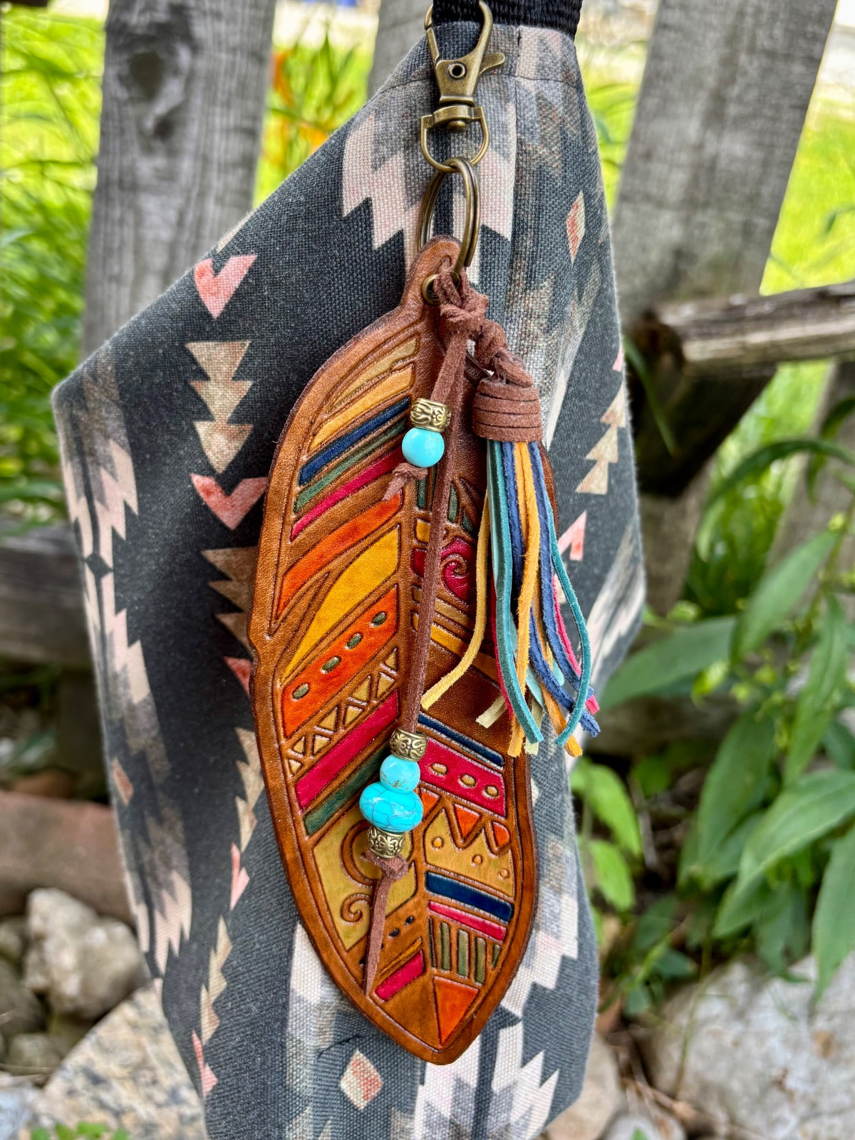 Tribal feather leather bag charm with tassel detail, clipped to a bronze swivel hook